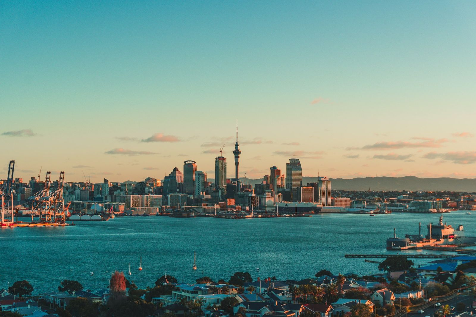 Auckland skyline and Sky Tower across the Waitematā Harbour under a warm low sun